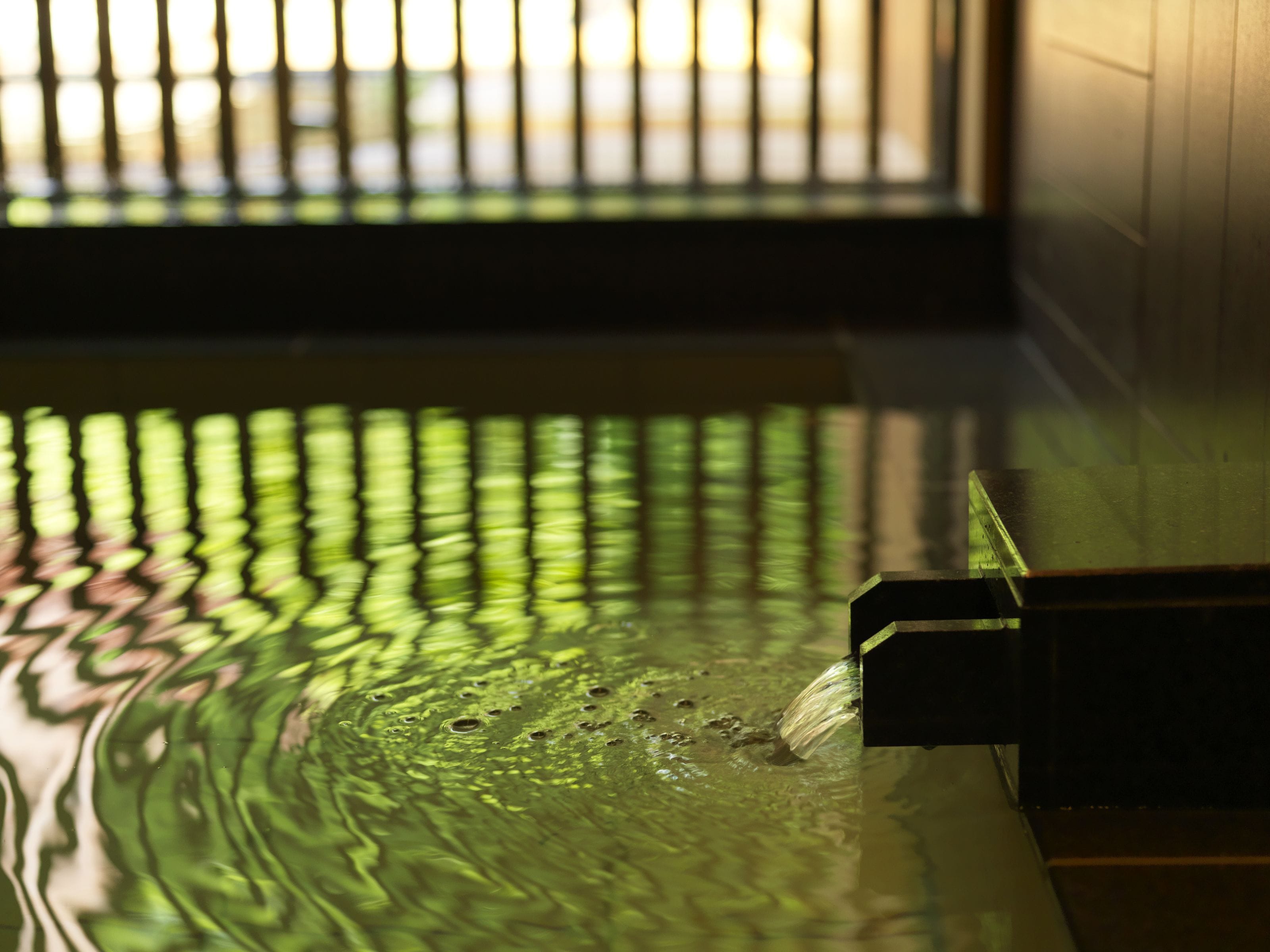 A water feature with a reflective surface, a metal structure, and a window in the background.