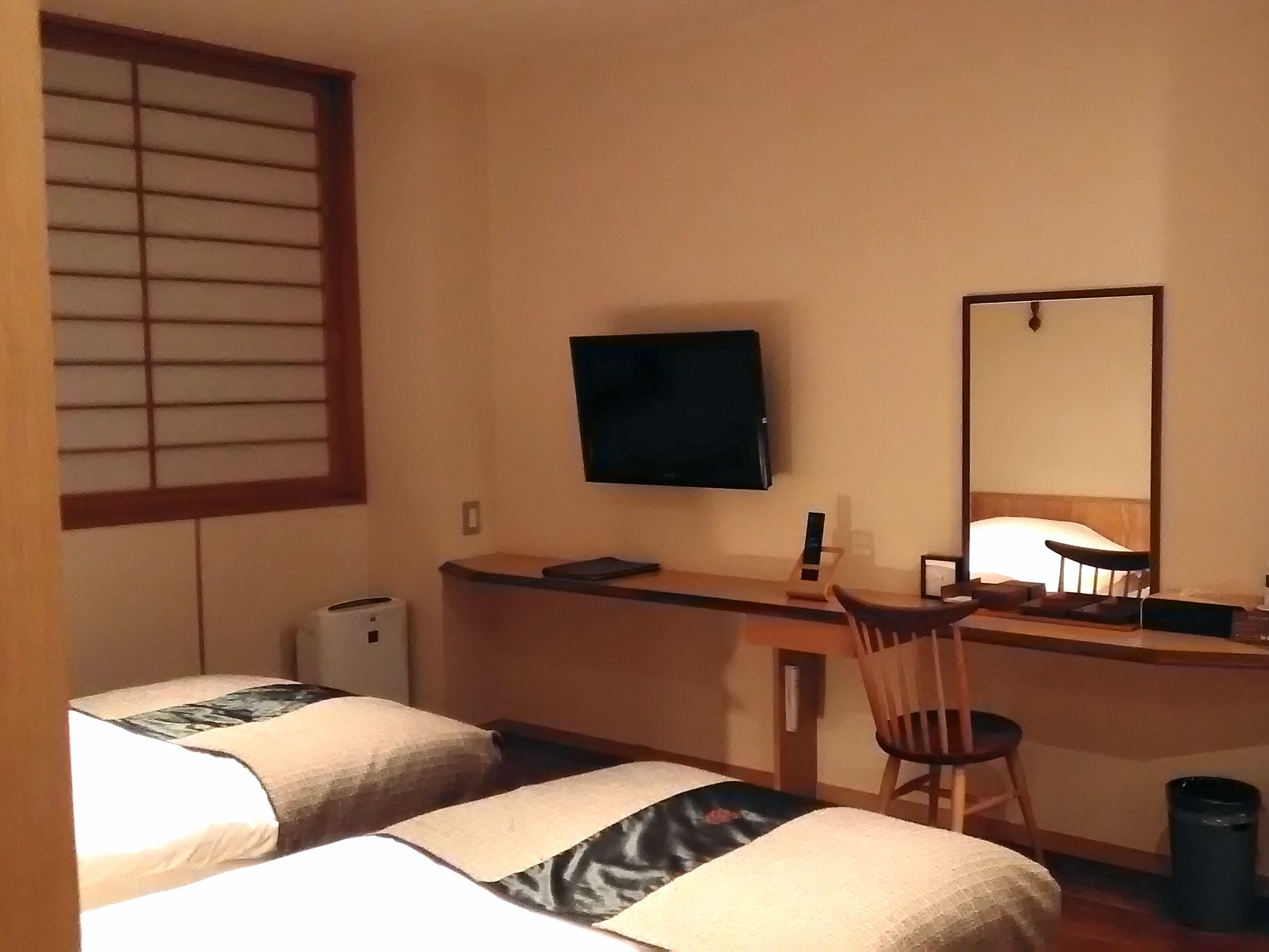 Ett hotellrum med en säng, ett skrivbord, en stol, en tv och en spegel.