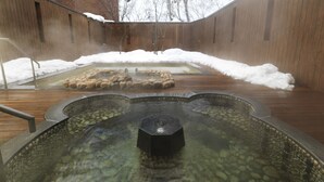 A hot spring area with wooden flooring, a stone hot tub, and a brick wall. - Niseko Konbu Onsen Tsuruga Besso Moku No Sho (Niseko)