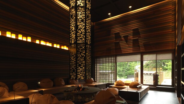 A modern interior with a wooden slatted ceiling, a central pillar with intricate patterns, and a seating area with cushions and a fire feature. - Niseko Konbu Onsen Tsuruga Besso Moku No Sho (Niseko)