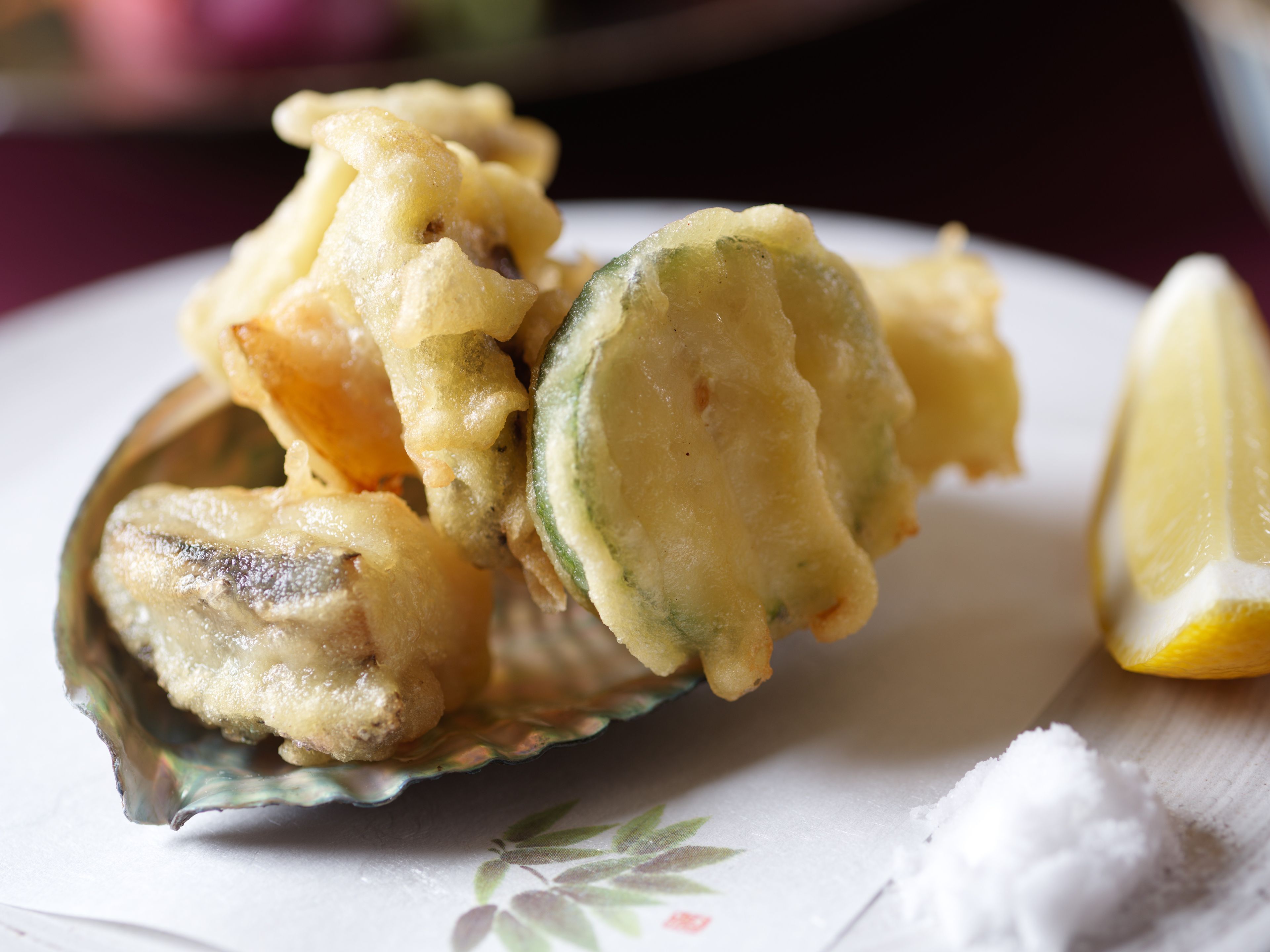 A plate of fried food with a lemon wedge and salt on the side.