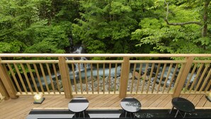 A wooden deck with a hot tub and two round tables, overlooking a flowing stream and lush greenery. - Niseko Konbu Onsen Tsuruga Besso Moku No Sho (Niseko)