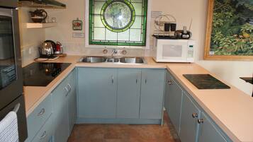 A kitchen with light blue cabinets, a stainless steel sink, a microwave, and a green stained glass window.