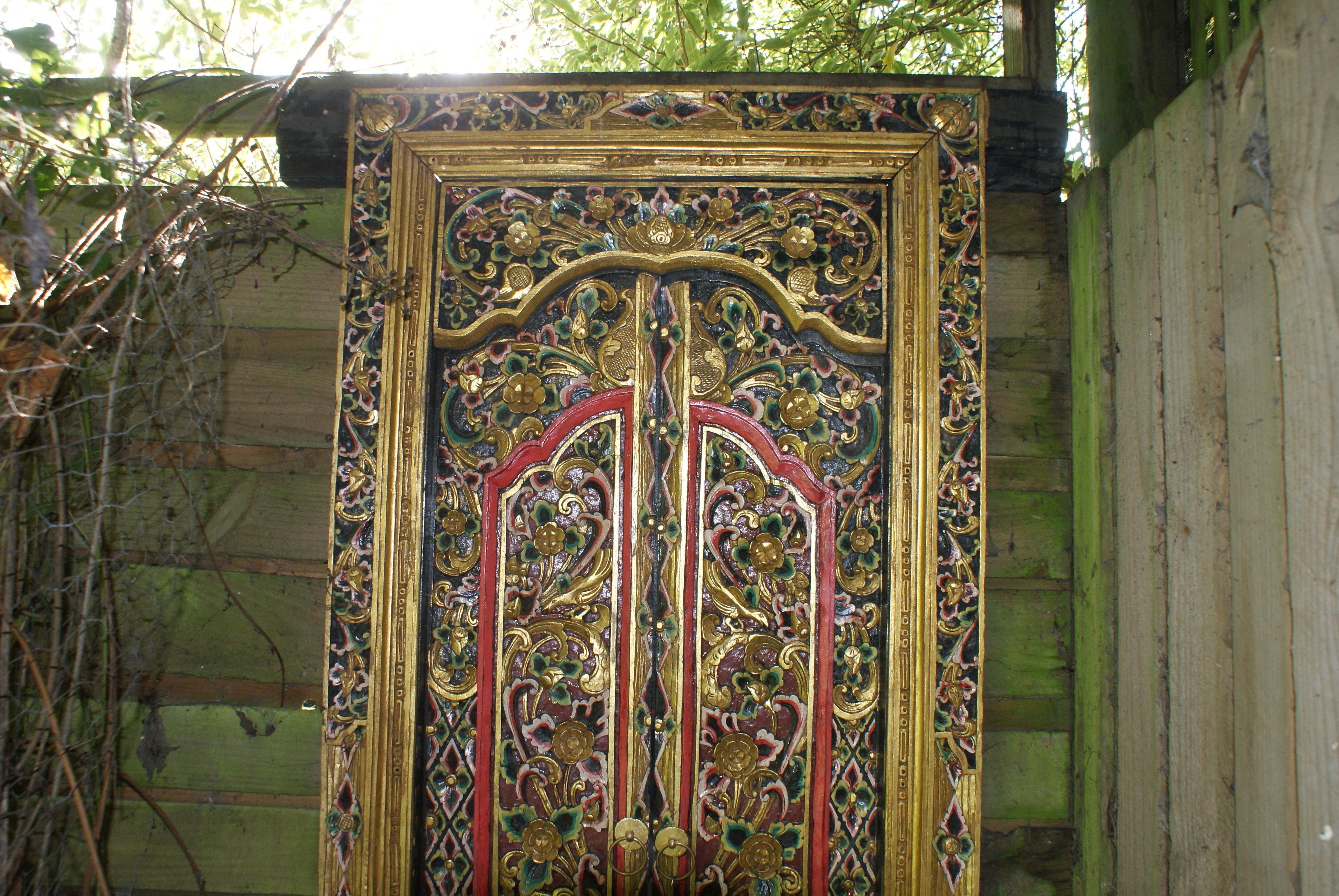 Une grande porte en bois richement décorée, ornée de sculptures complexes et dotée d’un cadre doré.