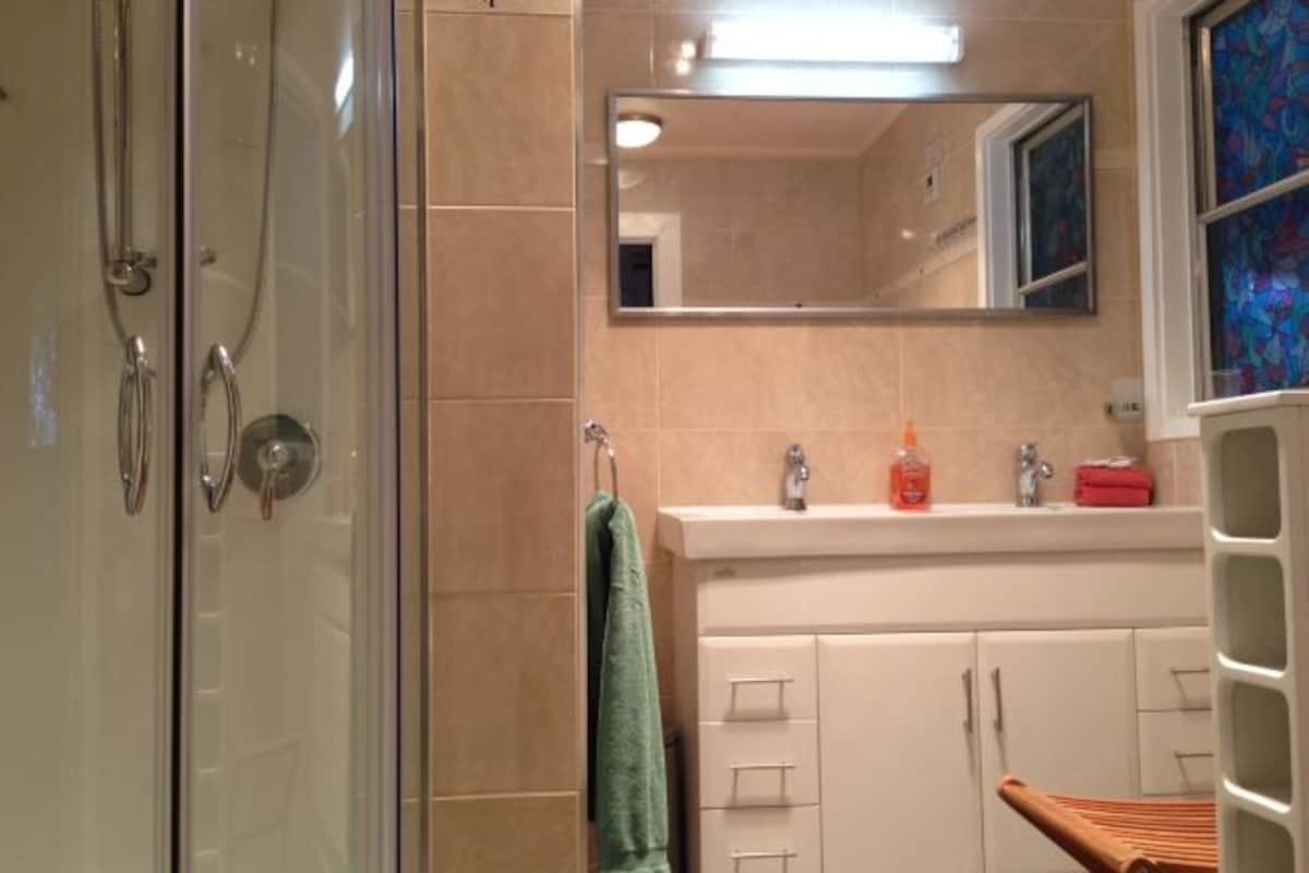 A bathroom with a glass shower enclosure, a sink with a mirror above it, and a towel hanging on a rack.