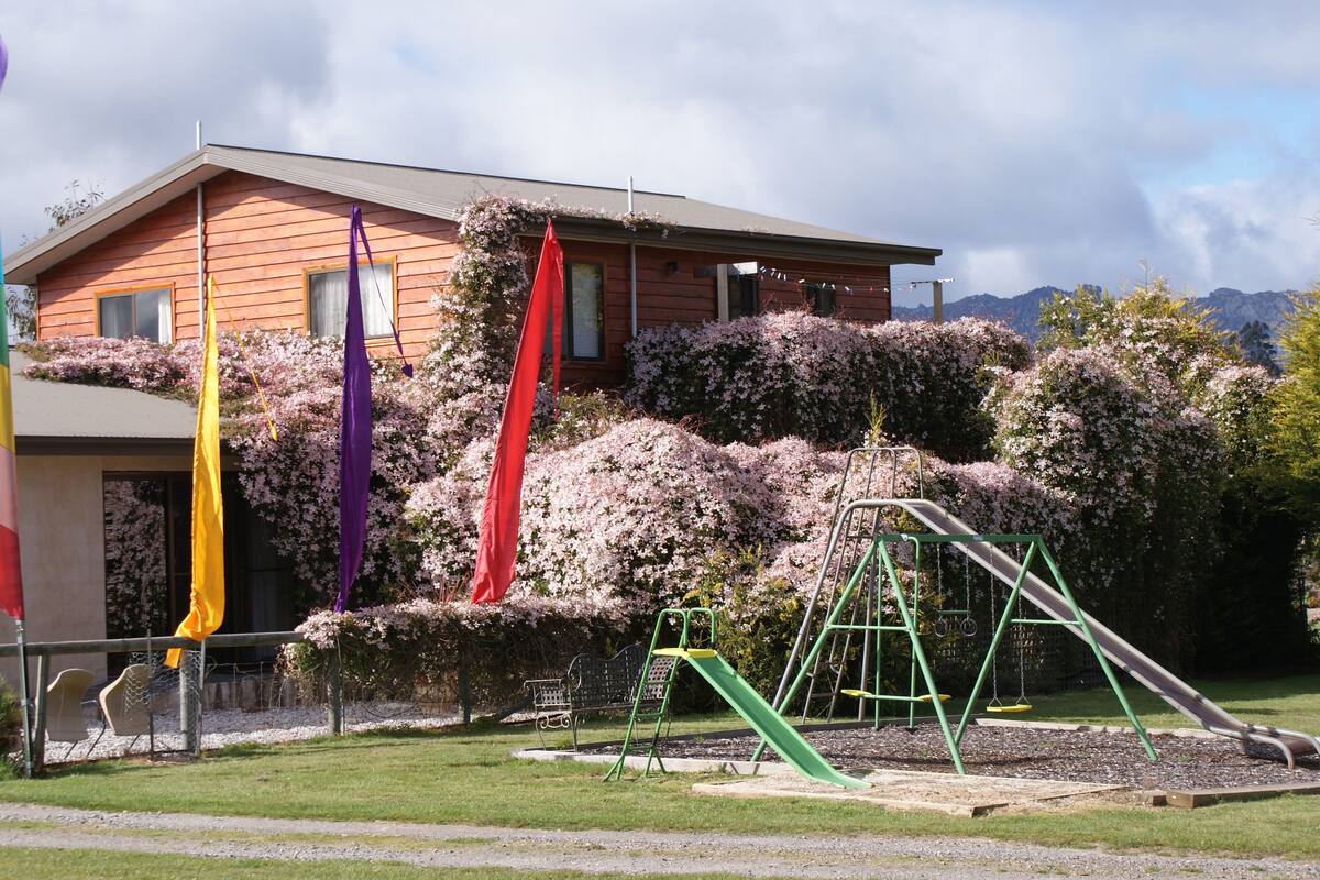 Una casa con fachada de madera, un porche y un parque infantil con tobogán y columpios.
