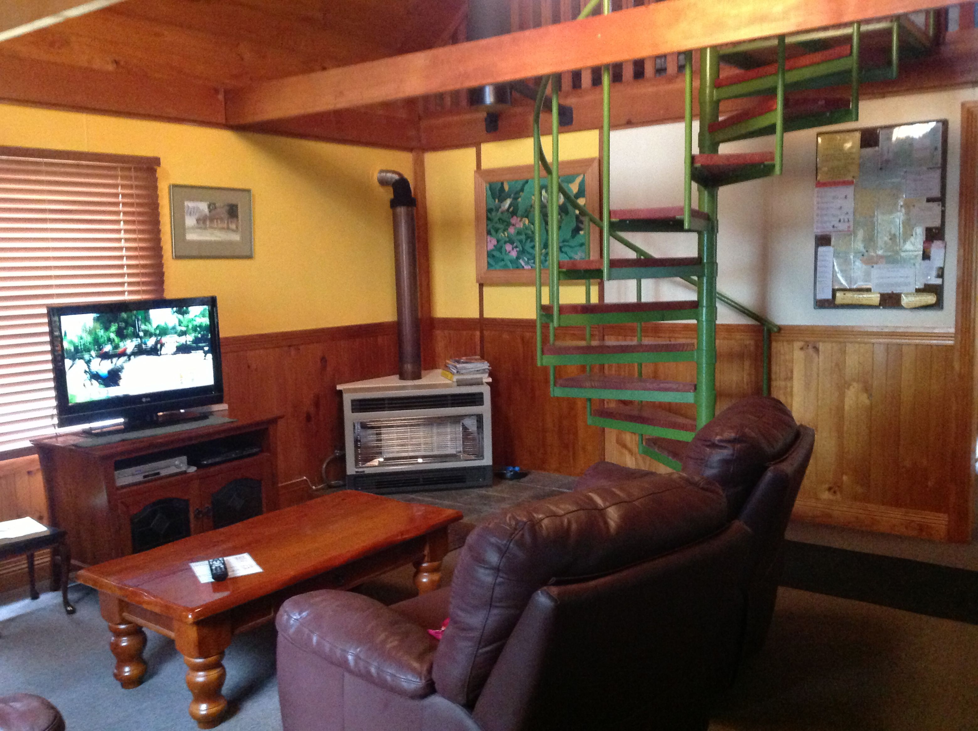 Una sala de estar con una escalera de madera, un televisor, una chimenea y un sofá de cuero.