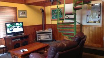 Una sala de estar con una escalera de madera, un televisor, una chimenea y un sofá de cuero.