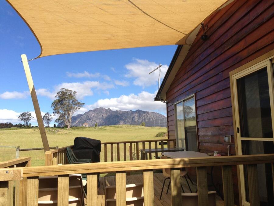 Eine Holzterrasse mit Tisch und Stühlen, einem Grill und Blick auf Berge im Hintergrund.