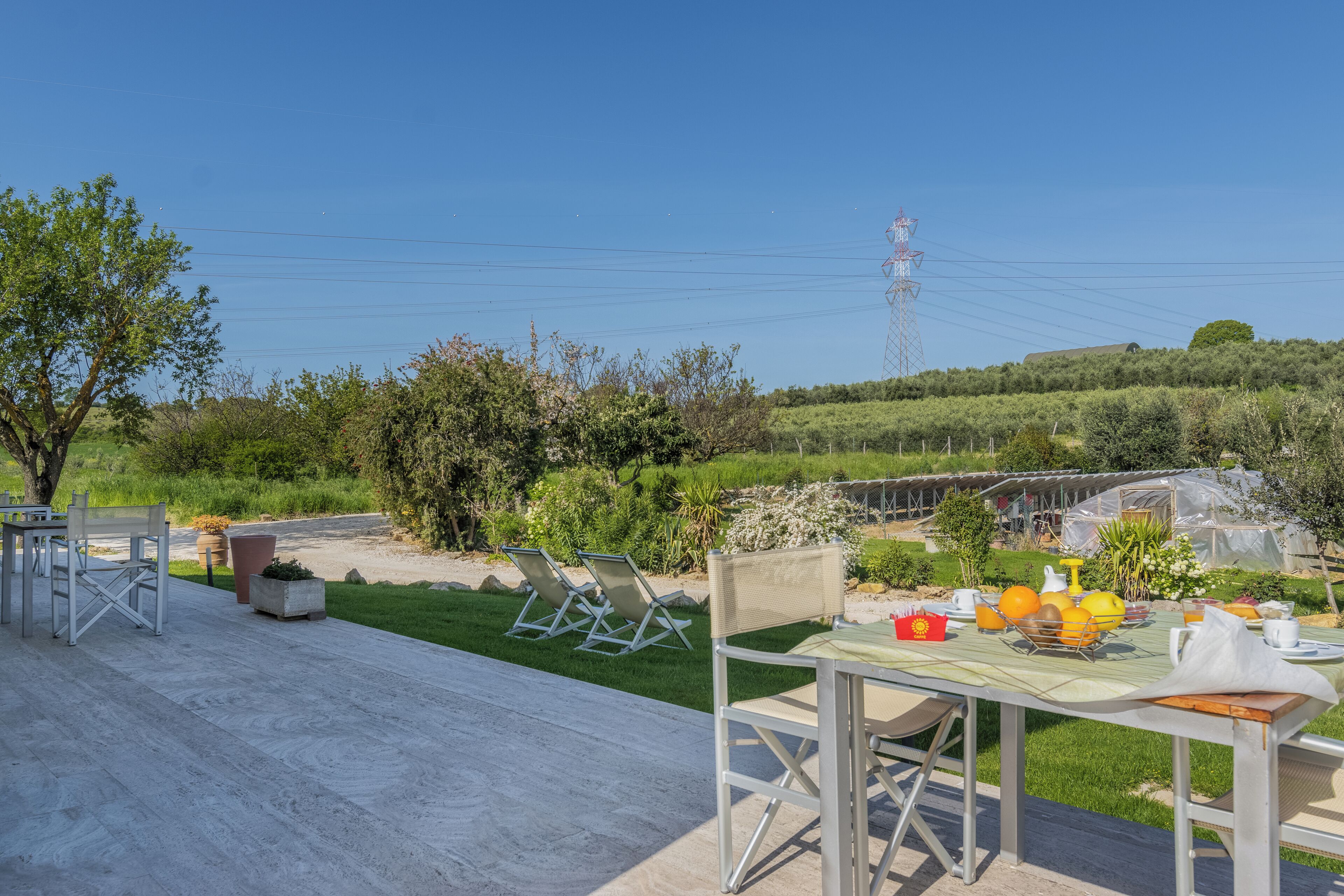 An outdoor dining area with a table set for breakfast, surrounded by greenery and a clear view of the countryside.