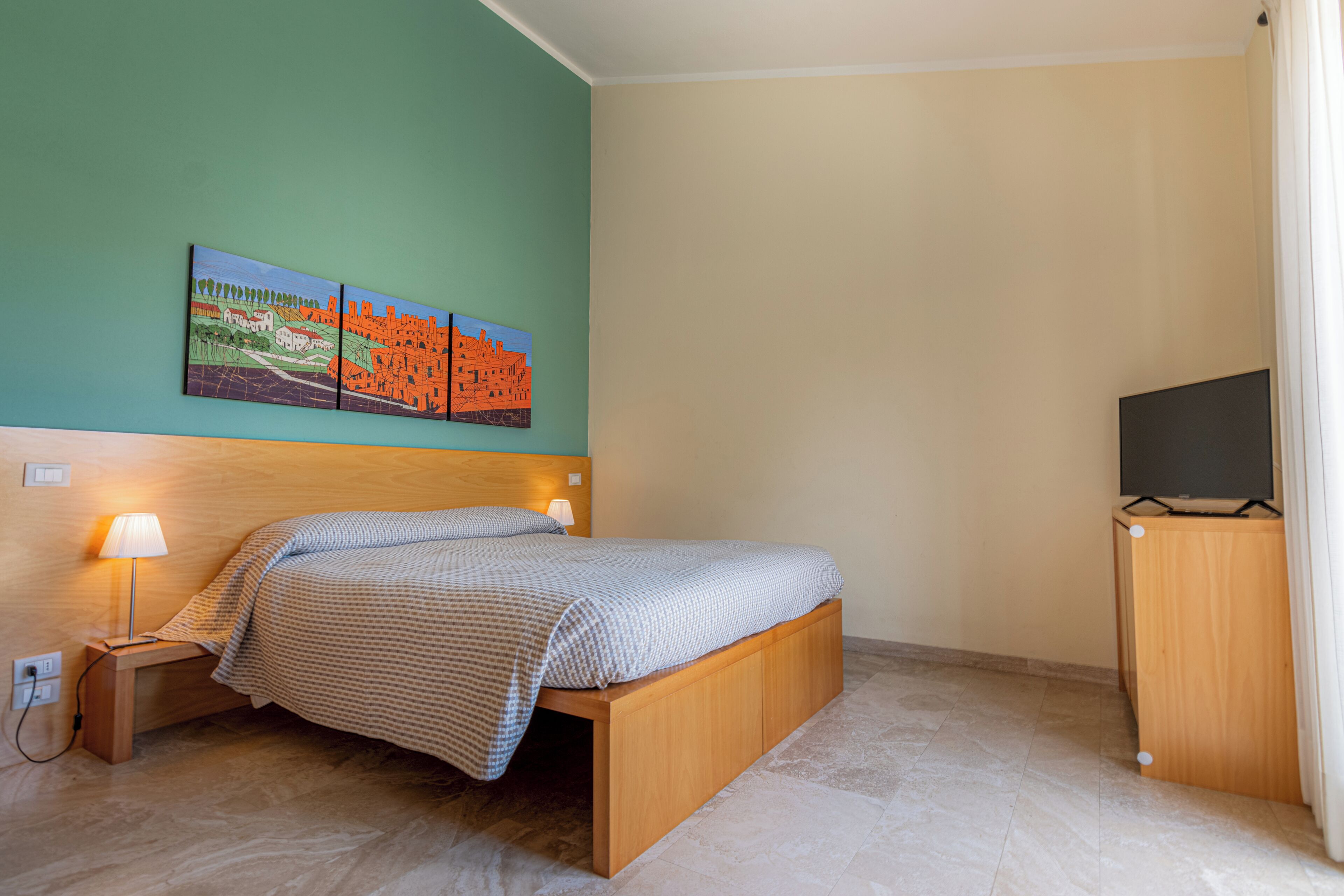 Une chambre à coucher avec un lit, une lampe de chevet, un meuble pour la télévision et un tableau accroché au mur.