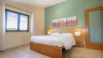 Quarto com cama, janela com cortinas, mesa de cabeceira e decoração nas paredes.