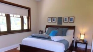 Quarto com cama de madeira, tapete branco e mesa de cabeceira com abajur.
