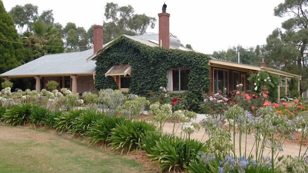 Uma casa com fachada coberta de hera verde, uma chaminé e um jardim com diversas flores.