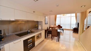 Cozinha moderna com forno embutido, micro-ondas e pia. Possui área de jantar com mesa e cadeiras, e uma grande janela que proporciona iluminação natural.