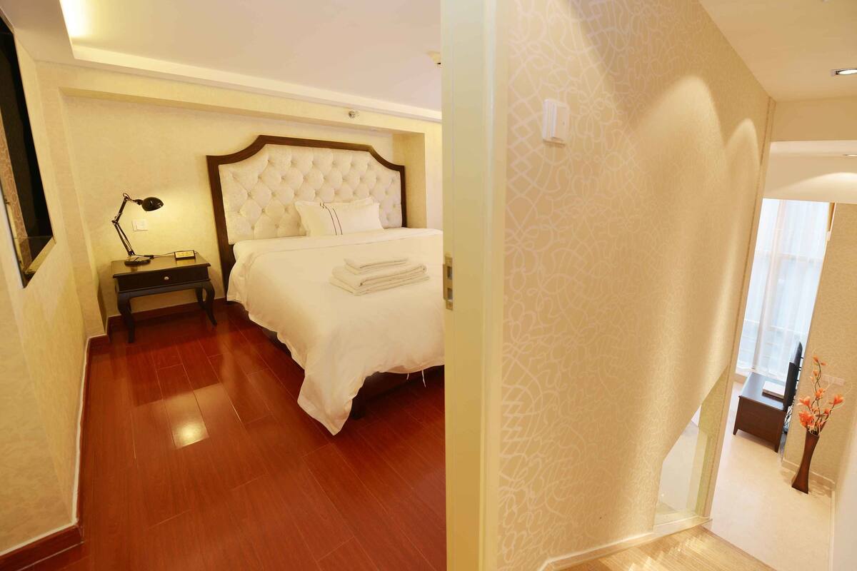 Une chambre d’hôtel avec un grand lit, une table de chevet avec une lampe et une vue sur le couloir.