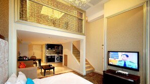 Quarto de hotel com uma cama grande, televisão, área de refeições e cozinha.