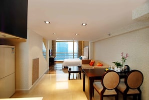 A hotel room with a bed, a sofa, a dining table with chairs, a TV, and a view of the city. - Guangzhou Grand View Golden Palace Apartment (Guangzhou)