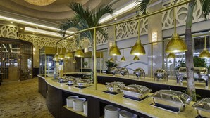 Buffet-alue, jossa on kullanväriset riippuvalaisimet, buffetpisteet ja koristeellinen seinä, jossa on palmu.