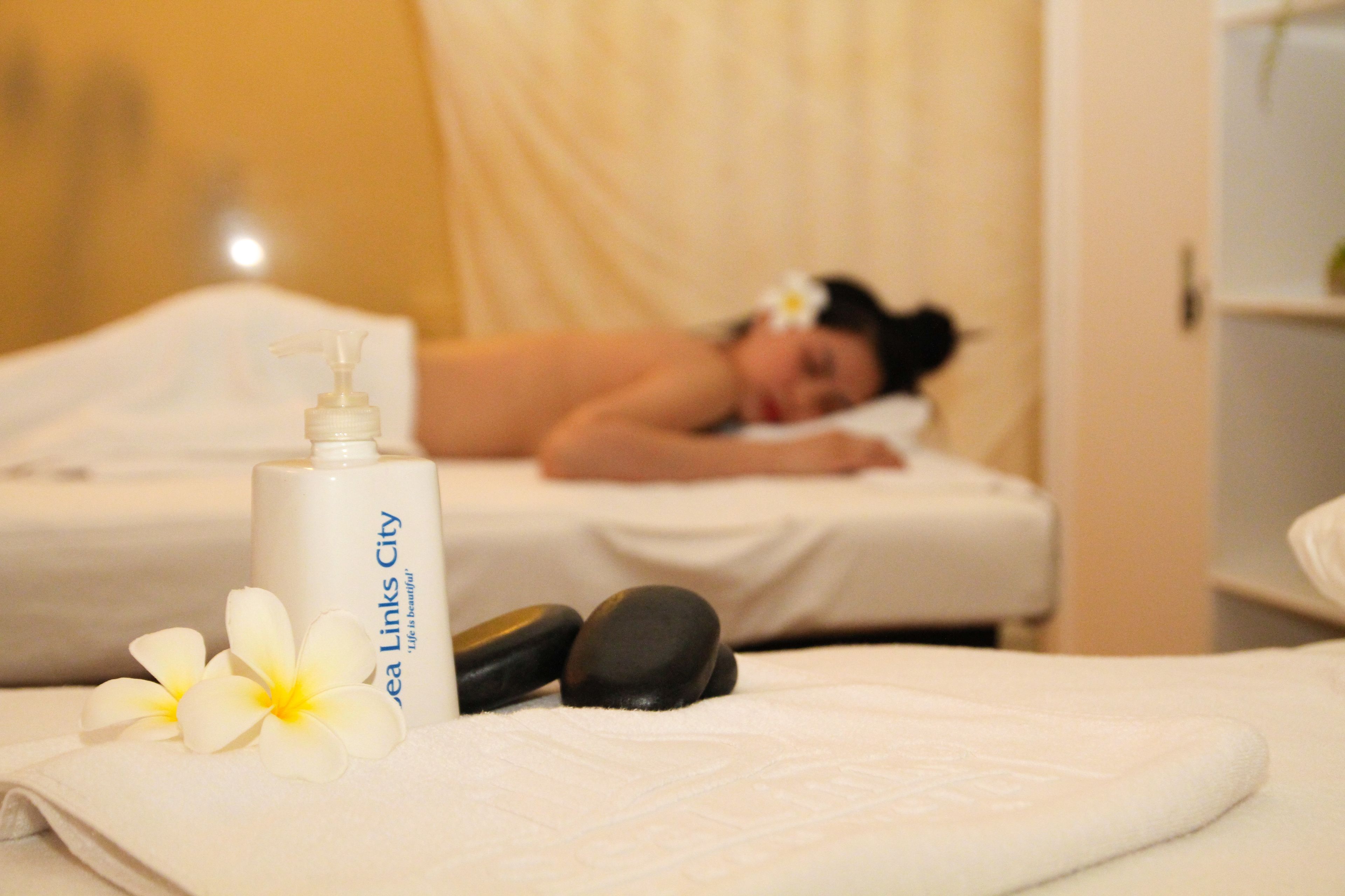 A spa setting with a massage table, a bottle of Sea Links City lotion, and two black stones.