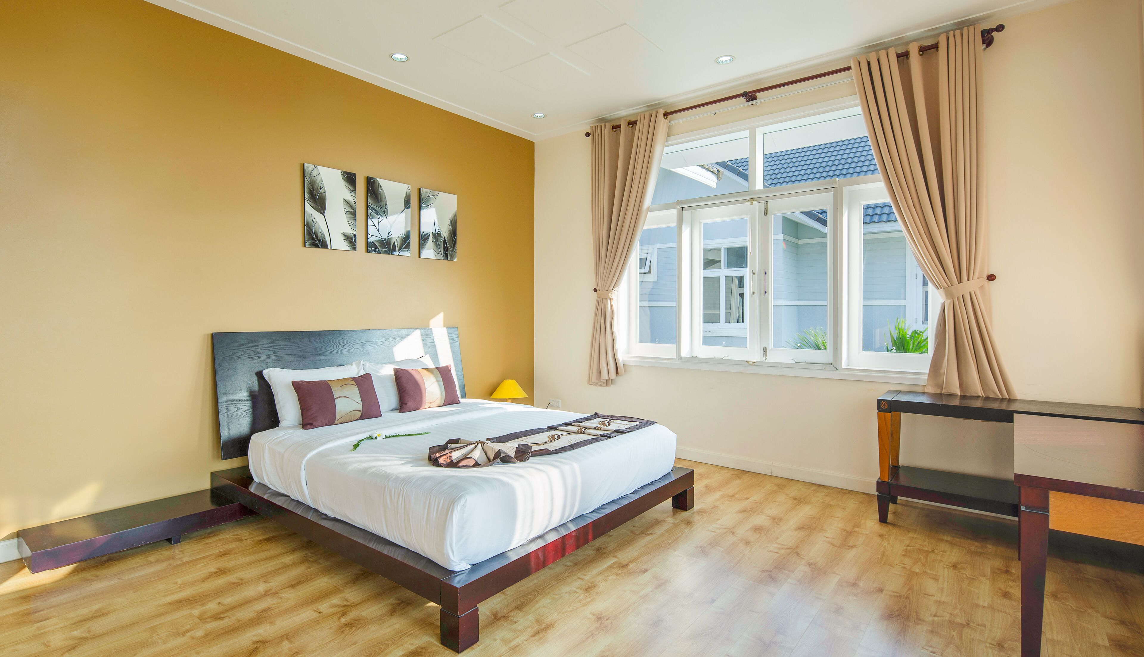 Ein Schlafzimmer mit einem Bett, einem Nachttisch, einem Fenster mit Vorhängen und Kunstwerken an der Wand.