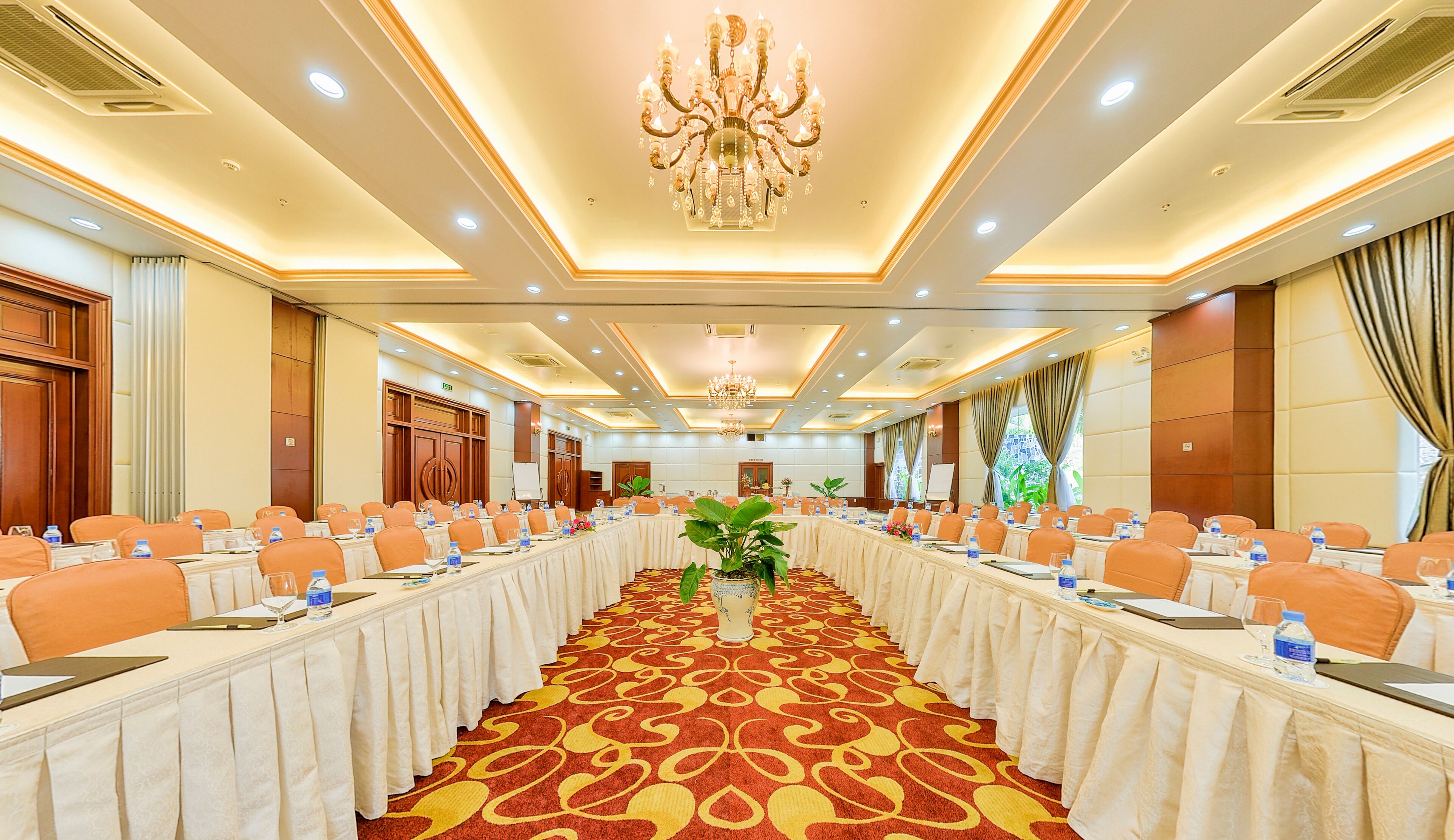Une salle de conférence avec une longue table, des chaises orange et un lustre.