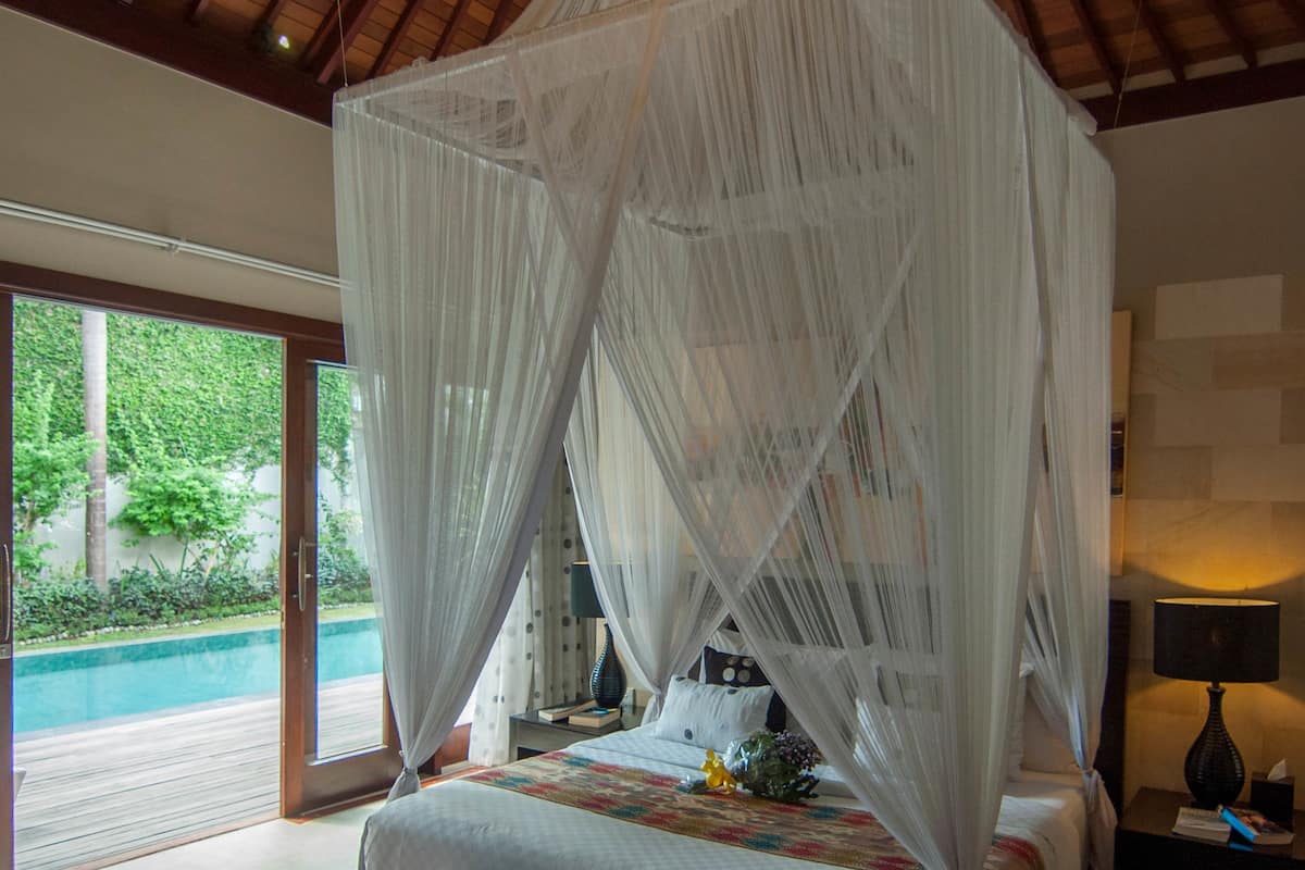 A bedroom with a canopy bed, a red patterned rug, and a view of a swimming pool.