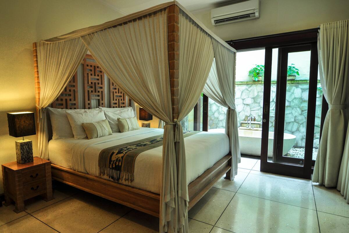 A four-poster canopy bed with a stone wall and a view of a garden through a glass door.