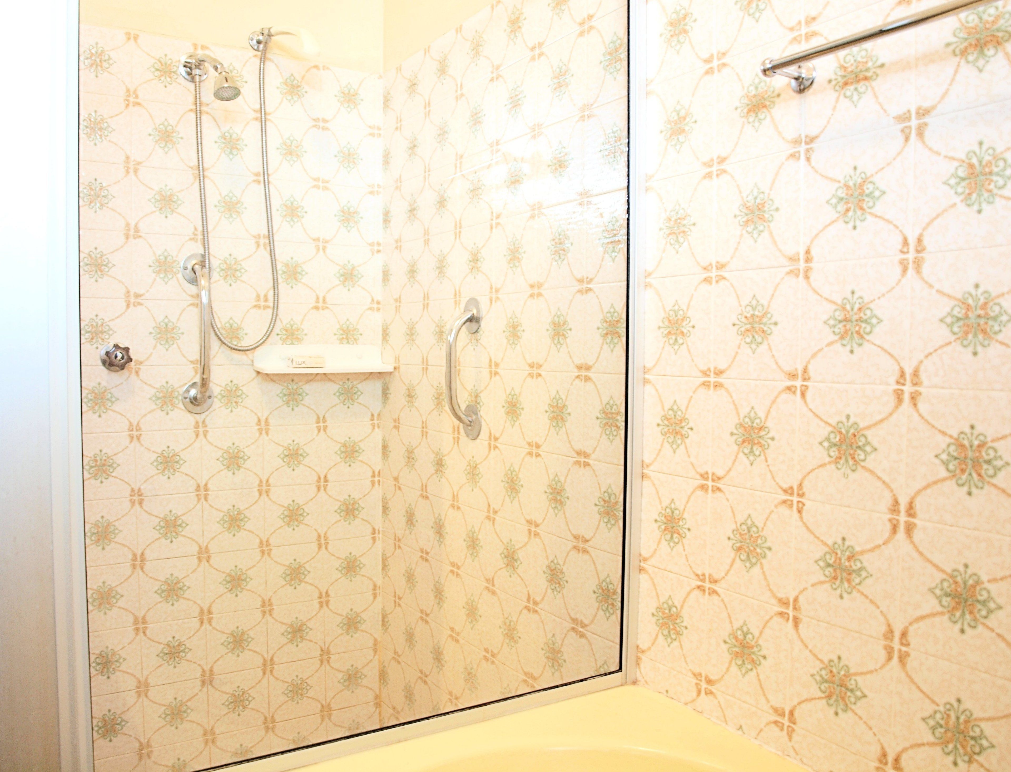 A shower area with a glass door, a handheld showerhead, and a wall-mounted towel rack.