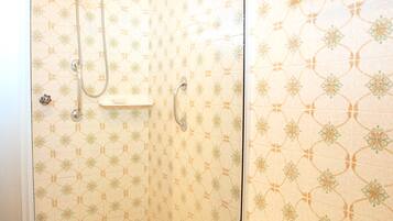 A shower area with a glass door, a handheld showerhead, and a wall-mounted towel rack.