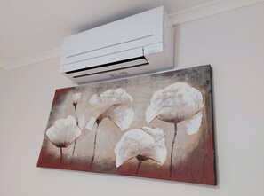 A wall-mounted air conditioner and a painting of flowers. - Capon Cottage (Broken Hill)