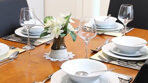 A dining table set with white plates, bowls, cutlery, and wine glasses, with a vase of white flowers in the center. - Capon Cottage (Broken Hill)