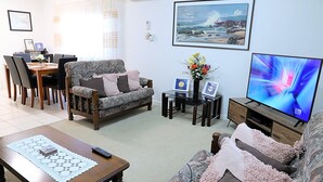 A living room with a sofa, a coffee table, a TV, and a dining area with chairs and a table. - Capon Cottage (Broken Hill)