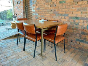 A brick-walled dining area with a wooden table and leather chairs. - Capon Cottage (Broken Hill)