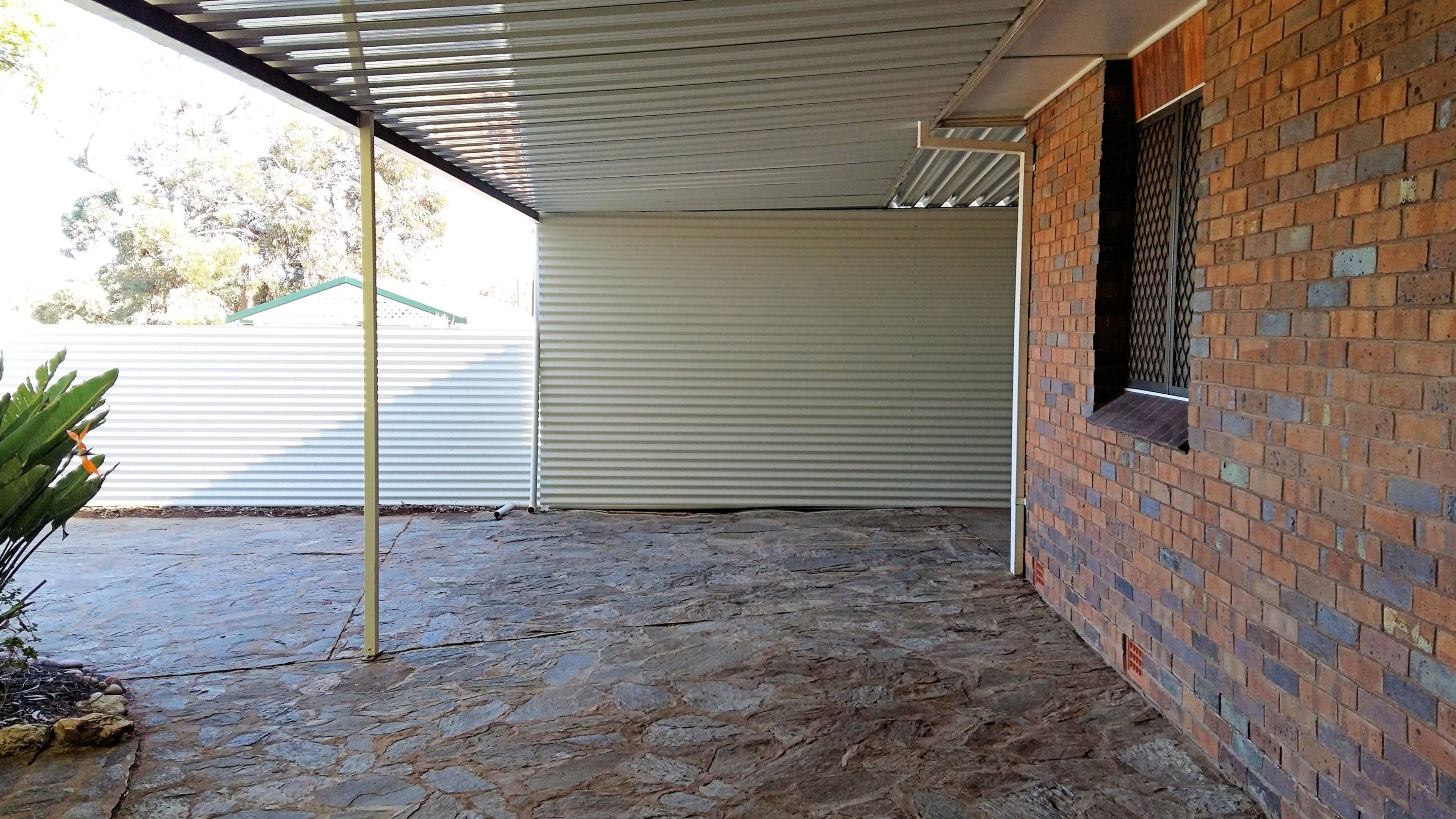 A covered outdoor area with a stone floor, a metal roof, and a brick wall.