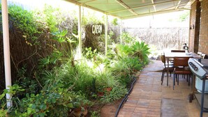 A covered patio with a brick floor, surrounded by lush greenery and a sign that reads "CAPON." - Capon Cottage (Broken Hill)