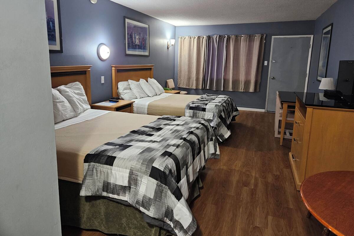 A hotel room with two beds, a desk, a chair, a lamp, and a door.