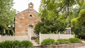 A stone building with a bell tower, surrounded by a white picket fence and lush greenery. - Clare Valley Heritage Retreat (Clare)