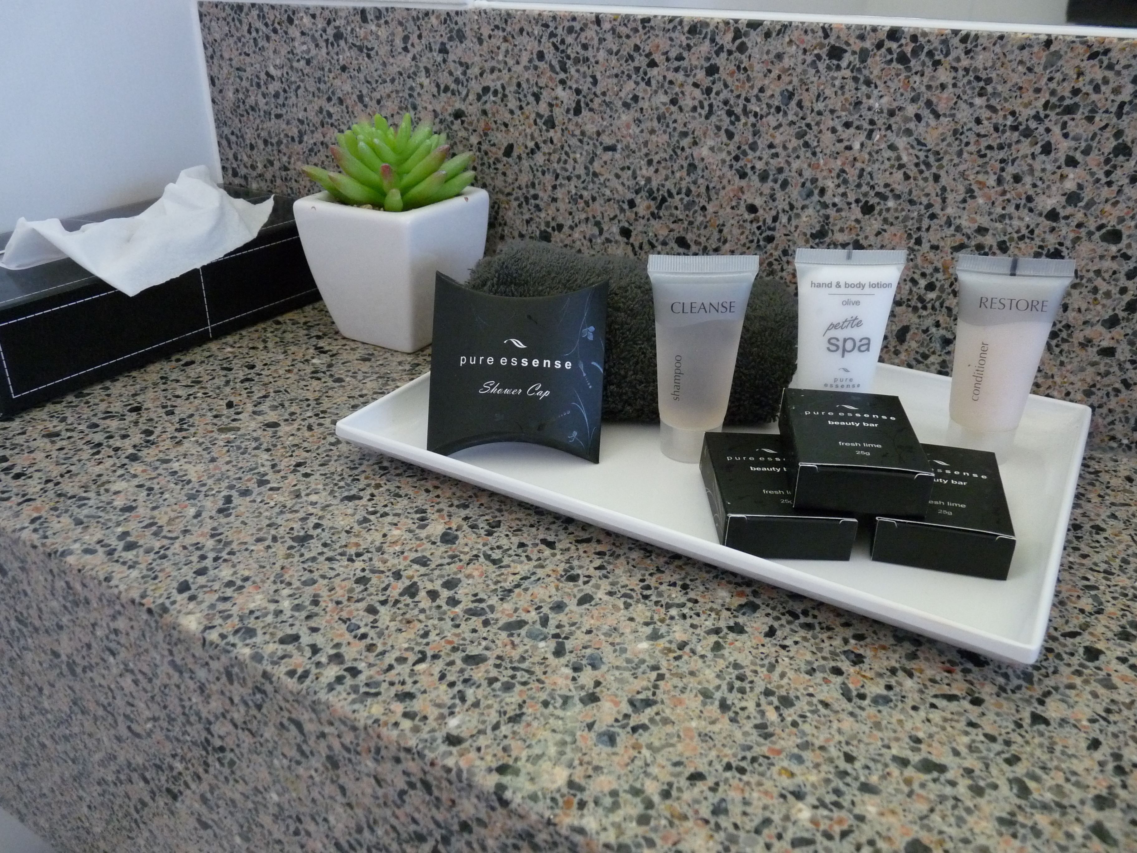 Una encimera de baño con diversos artículos de aseo, como un gorro de ducha, champú, loción para manos y cuerpo, acondicionador y jabón de belleza.