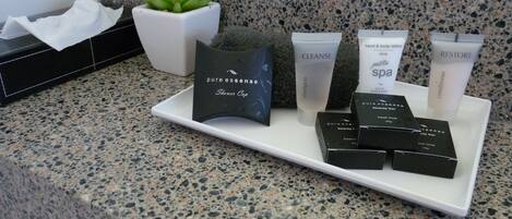 A bathroom counter with various toiletries including a shower cap, shampoo, hand and body lotion, conditioner, and a beauty bar.