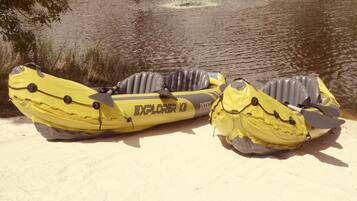 Dos kayaks inflables amarillos con la etiqueta 'EXPLORER K2' sobre una orilla arenosa junto a un cuerpo de agua.