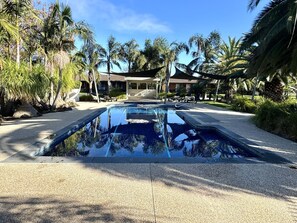 A swimming pool with a clear view of the surrounding area, including palm trees and a building with a covered patio. - Barwon Valley Lodge (Belmont)