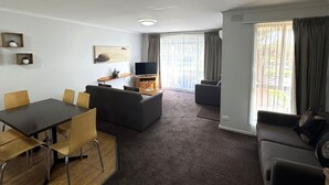 A modern living room with a dining area, a flat-screen TV, and a large window with curtains. - Barwon Valley Lodge (Belmont)