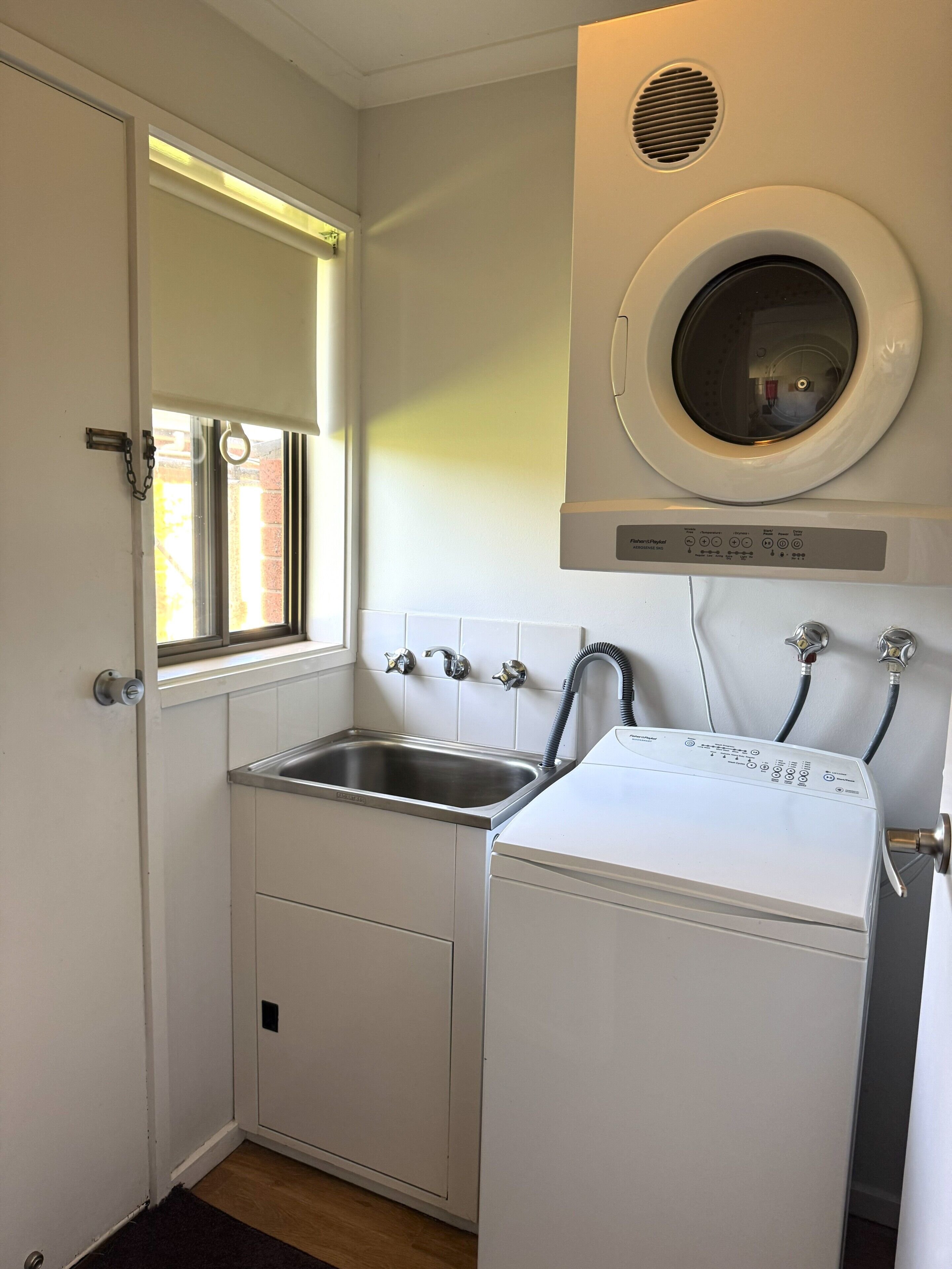 A compact laundry room with a washing machine, a sink, and a window.