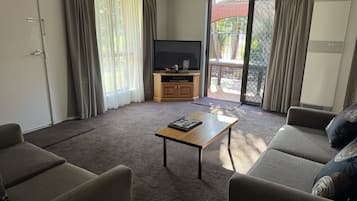 A living room with a sofa, a coffee table, a TV, and a sliding glass door leading to an outdoor area.