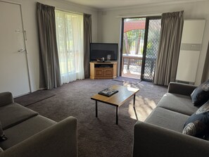 A living room with a sofa, a coffee table, a TV, and a sliding glass door leading to an outdoor area. - Barwon Valley Lodge (Belmont)