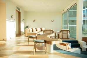 Uma sala de estar moderna com uma mesa de madeira arredondada, assentos confortáveis e uma grande janela que traz luz natural.