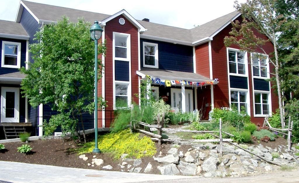 A two-story house with a red exterior, white trim, and a front porch. There is a small garden with rocks and plants.