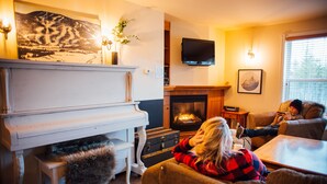 A cozy living room with a fireplace, a piano, and a television. - Maison de Vébron (L'Anse-Saint-Jean)