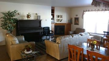 A living room with a piano, sofas, a dining table with chairs, and a fireplace.